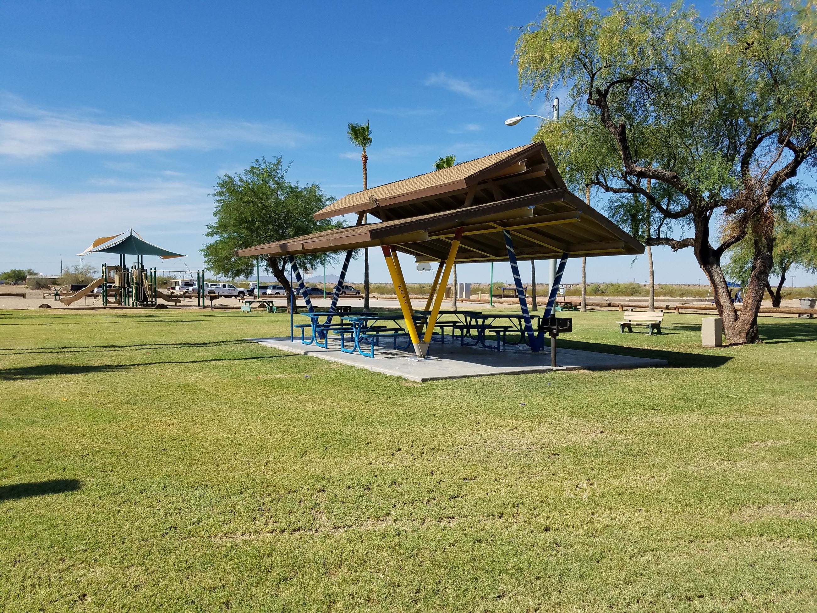 Ramada with playground in distance and grassy field at Gila Bend Rotary Park